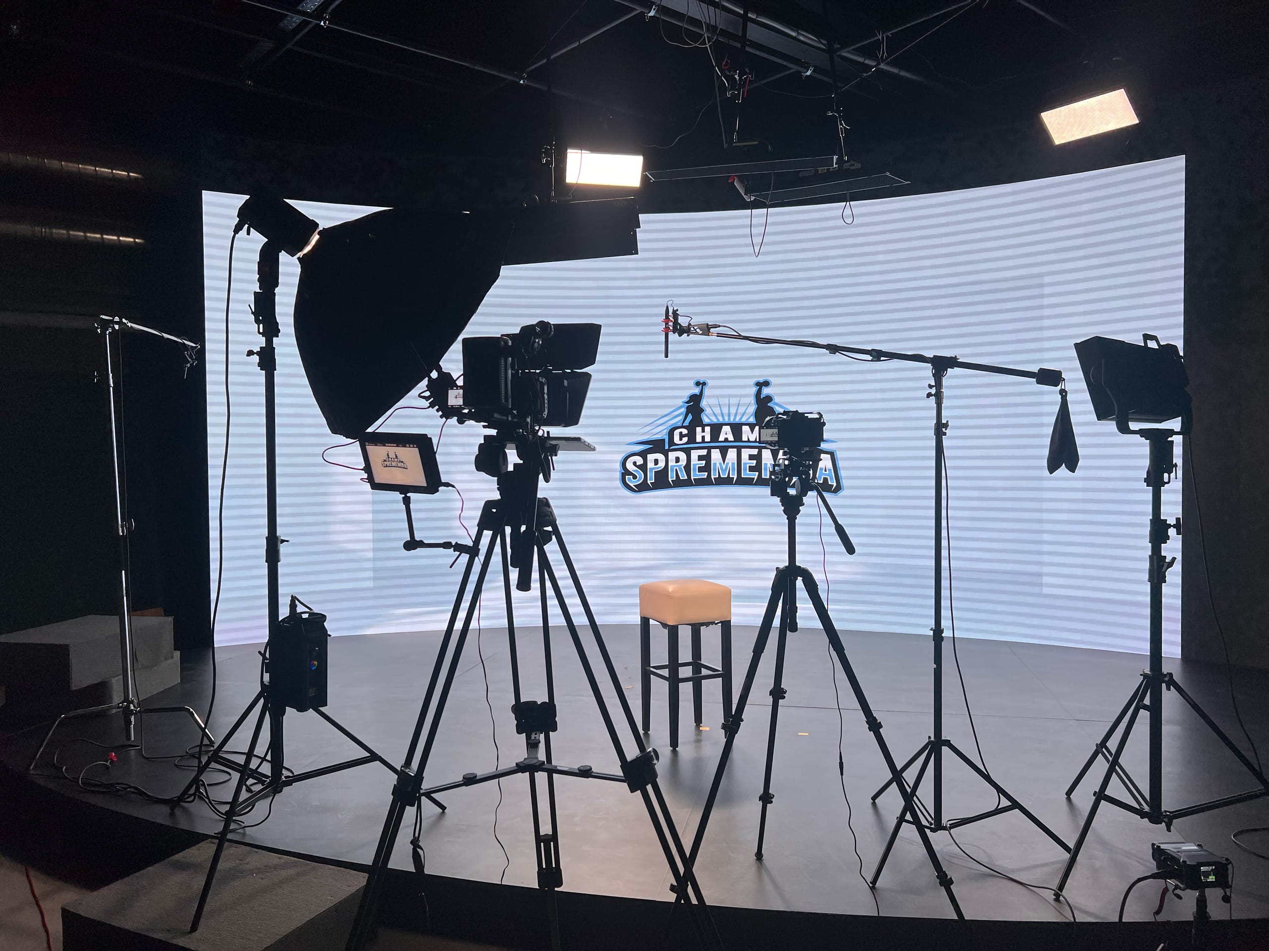Televizijski studio z lučmi, kamero in mikrofonom pred LED zaslonom.