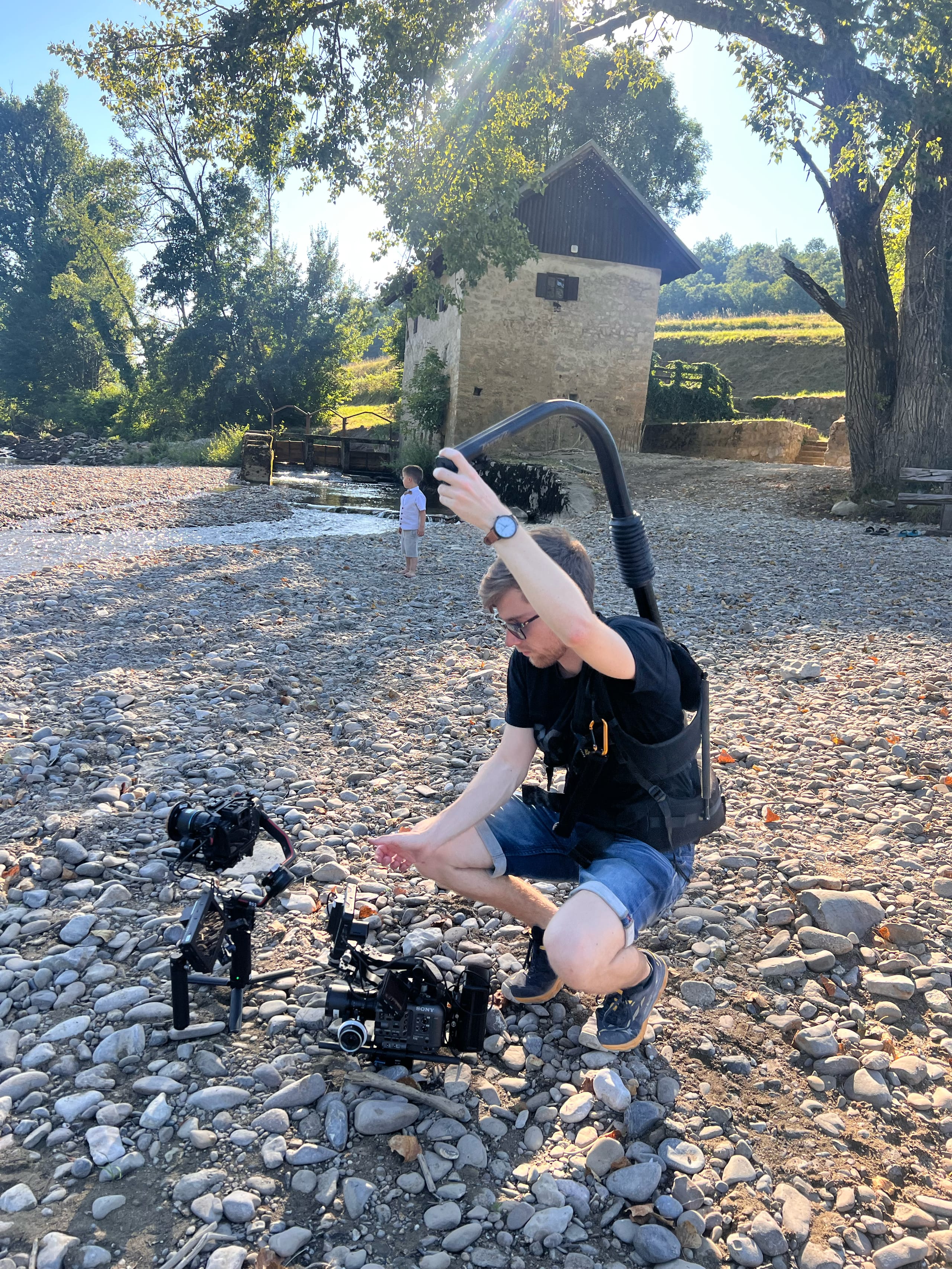 Snemalec s stabilizatorjem kamere sedi na prodnati obali reke.
