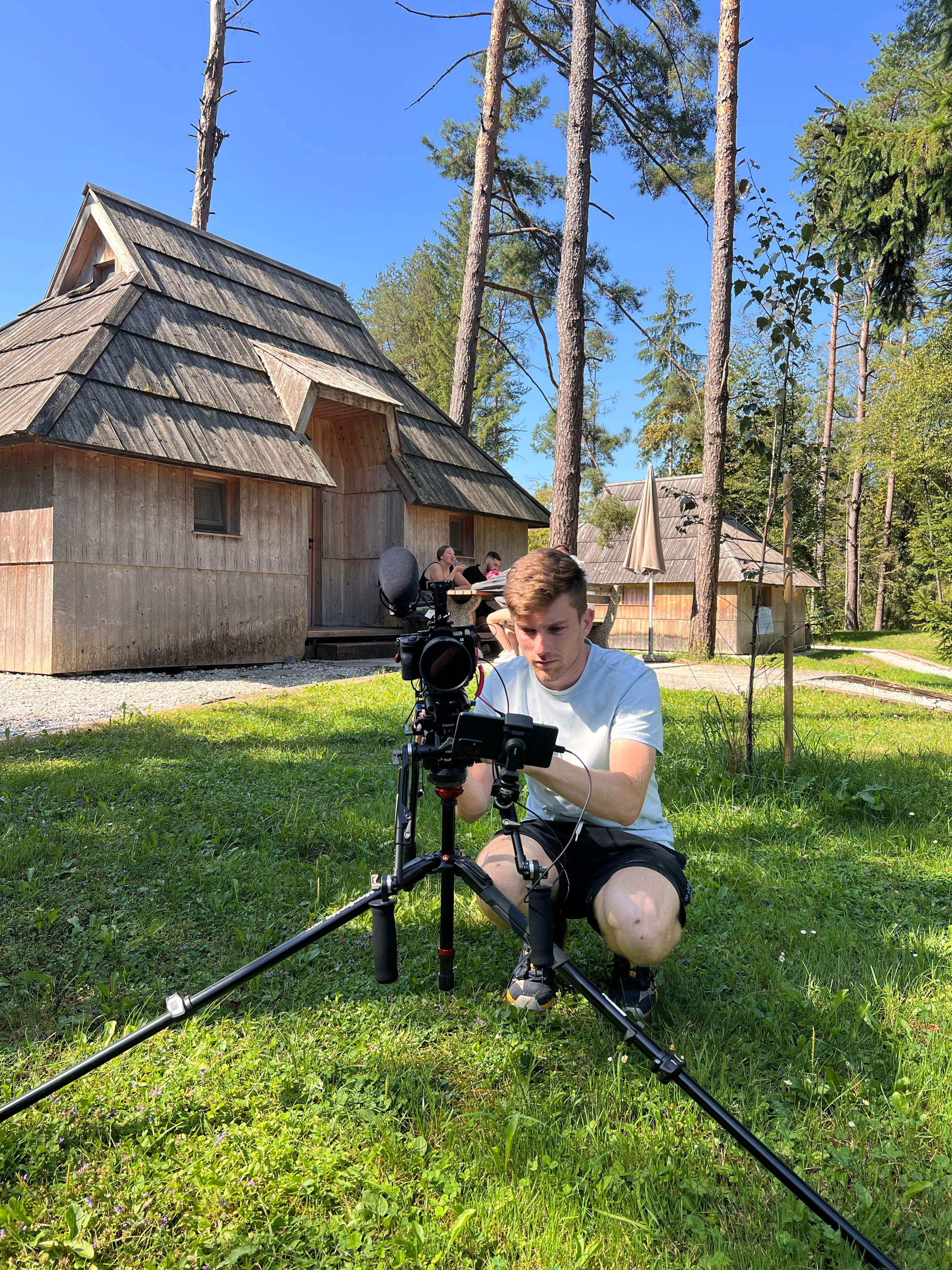 Snemalna ekipa s kamero na stabilizatorju pred leseno kočo v naravi.