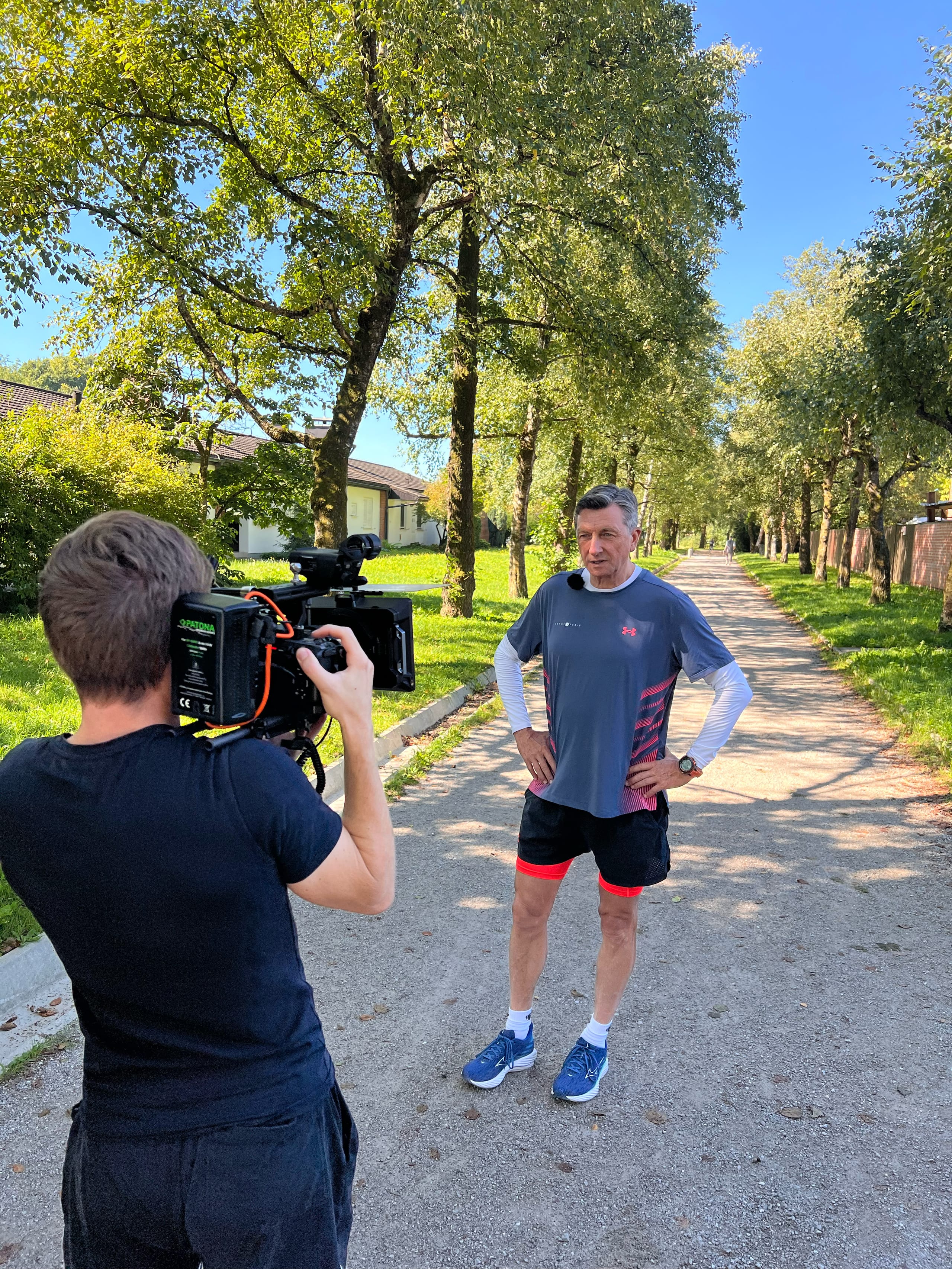 Snemalec s kamero snema moškega v športni opremi na sprehajalni poti.