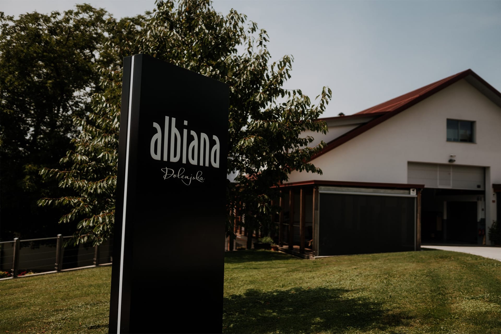 Črna tabla z napisom Albiana pred hišo s travnikom in drevesom