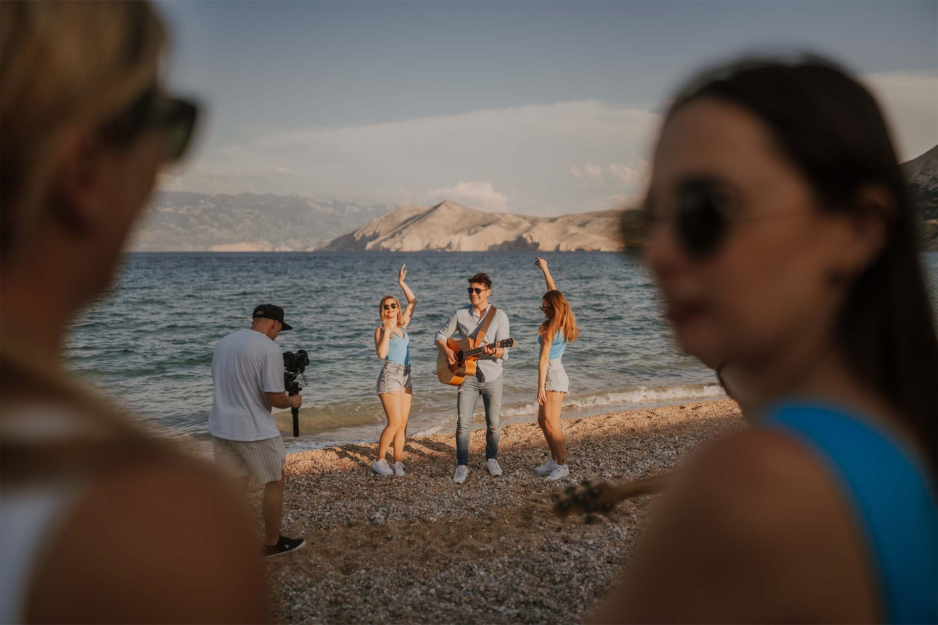 Snemanje glasbenega videa na obali, kitarist in plesalki ob morju