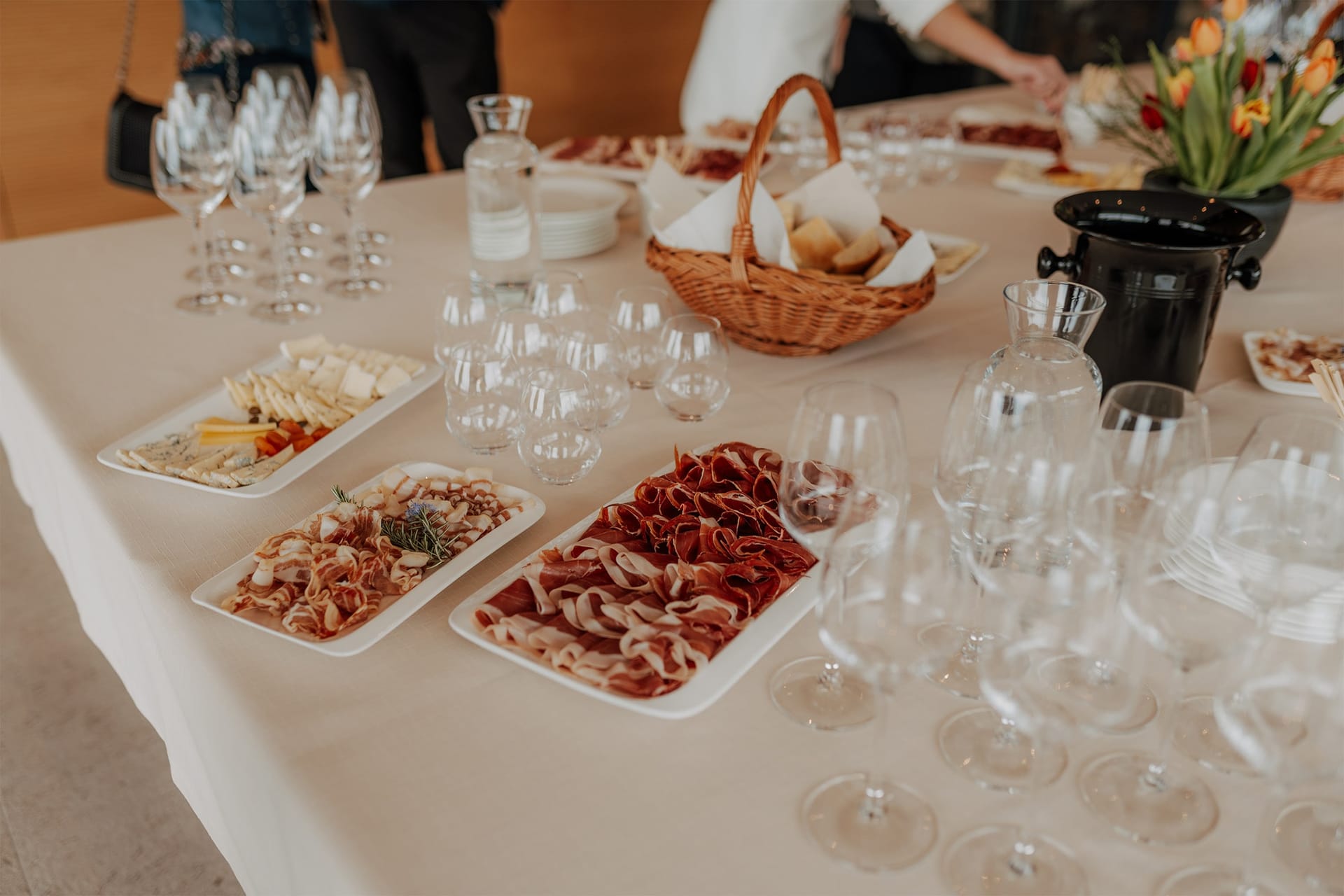 Miza s pogrinjkom, pladnji pršuta in sirov ter kozarci za vino.