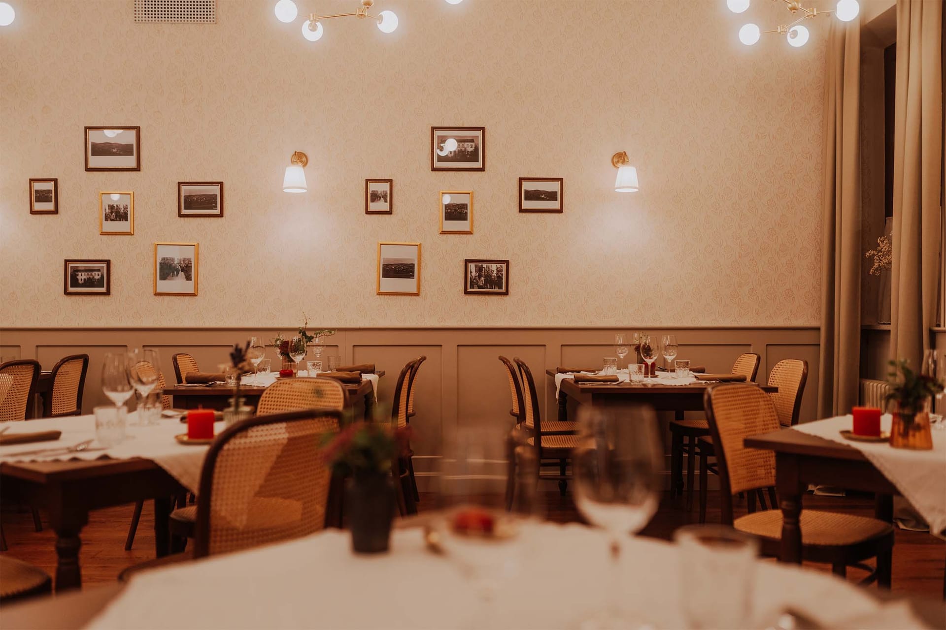 Notranjost restavracije s pogrnjenimi mizami in črno-belimi fotografijami na steni.