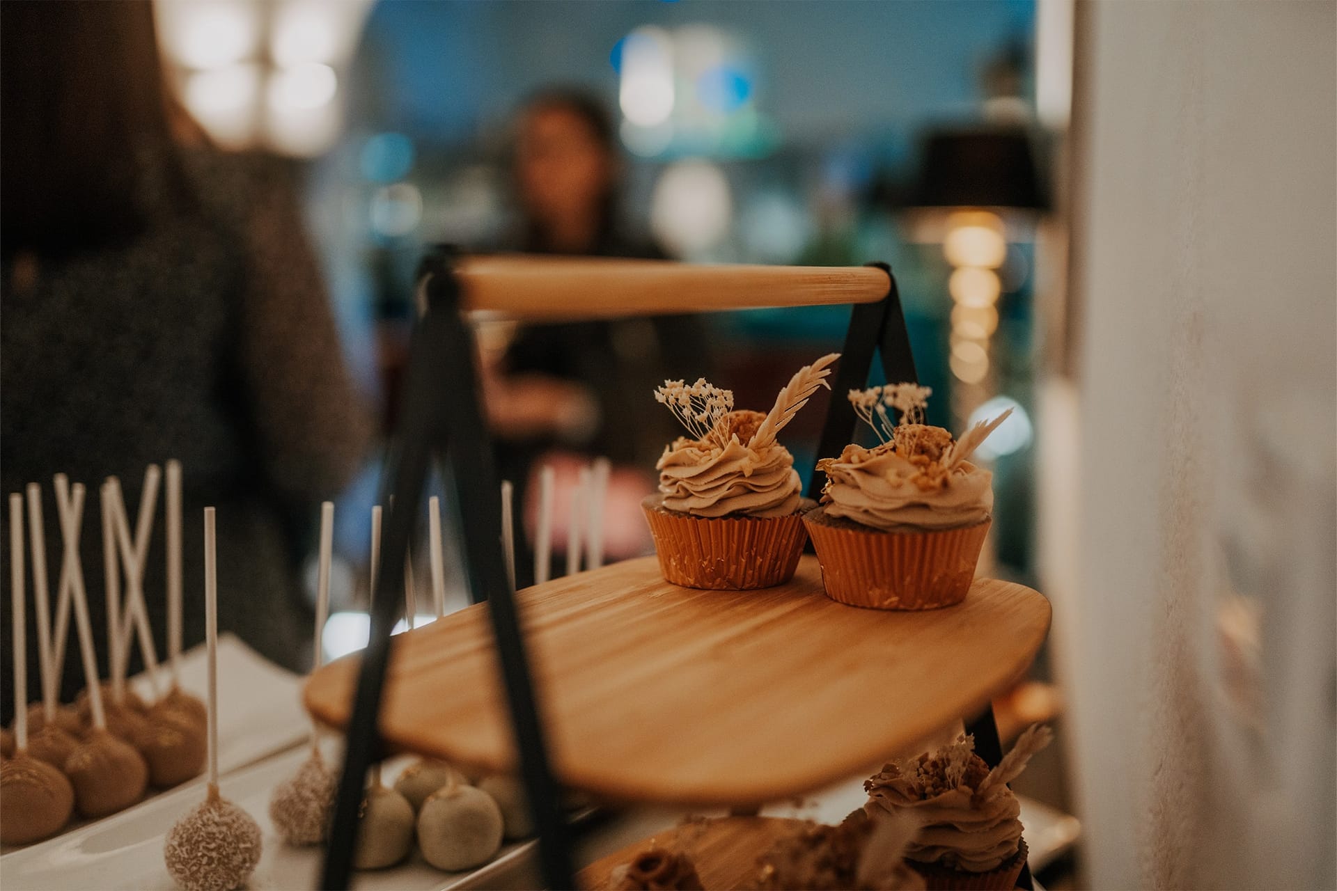 Muffini z belo čokolado na leseni mizici, v ozadju zamegljeni gostje.
