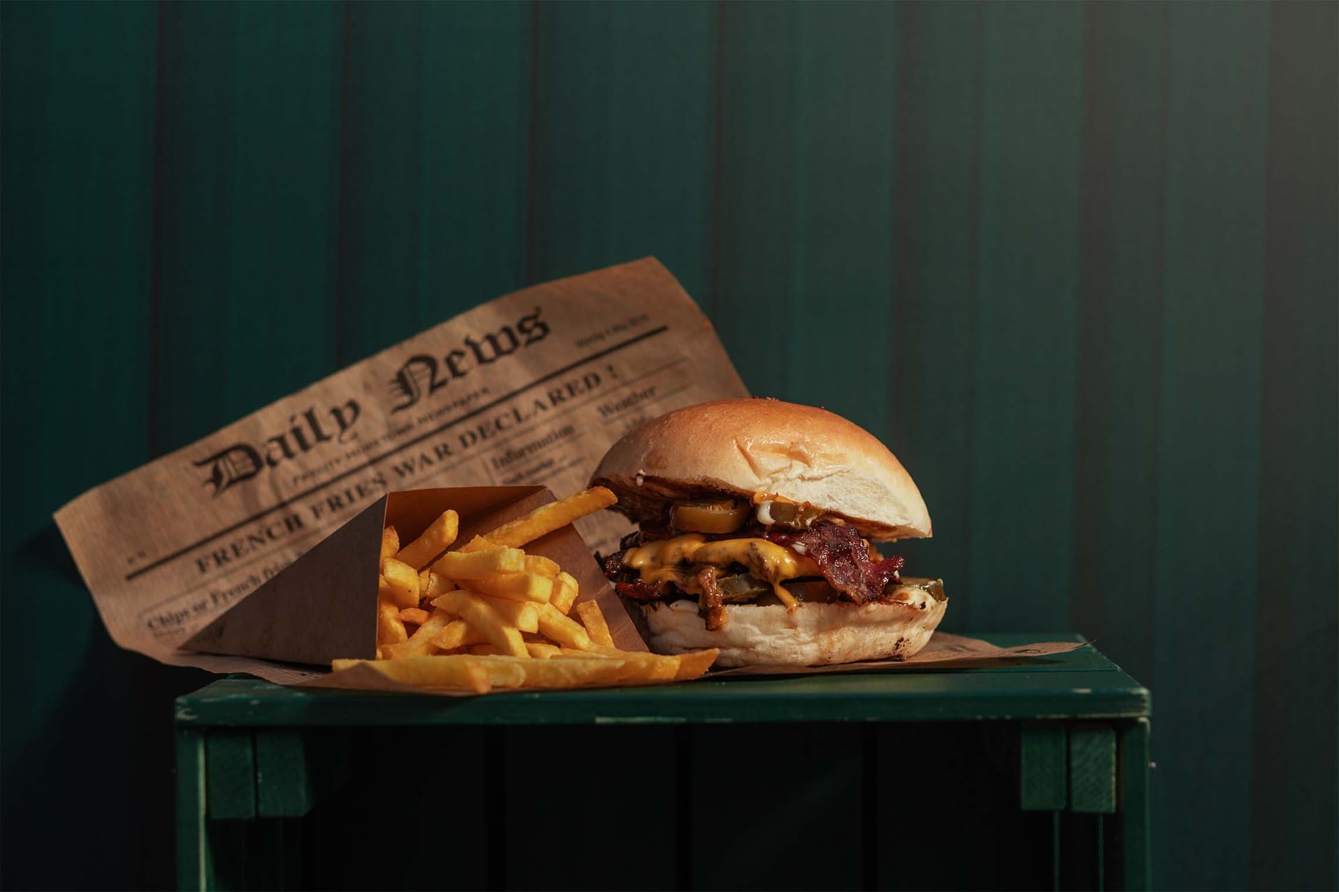 Burger in ocvrt krompirček v časopisnem papirju na leseni zaboj postavljena.