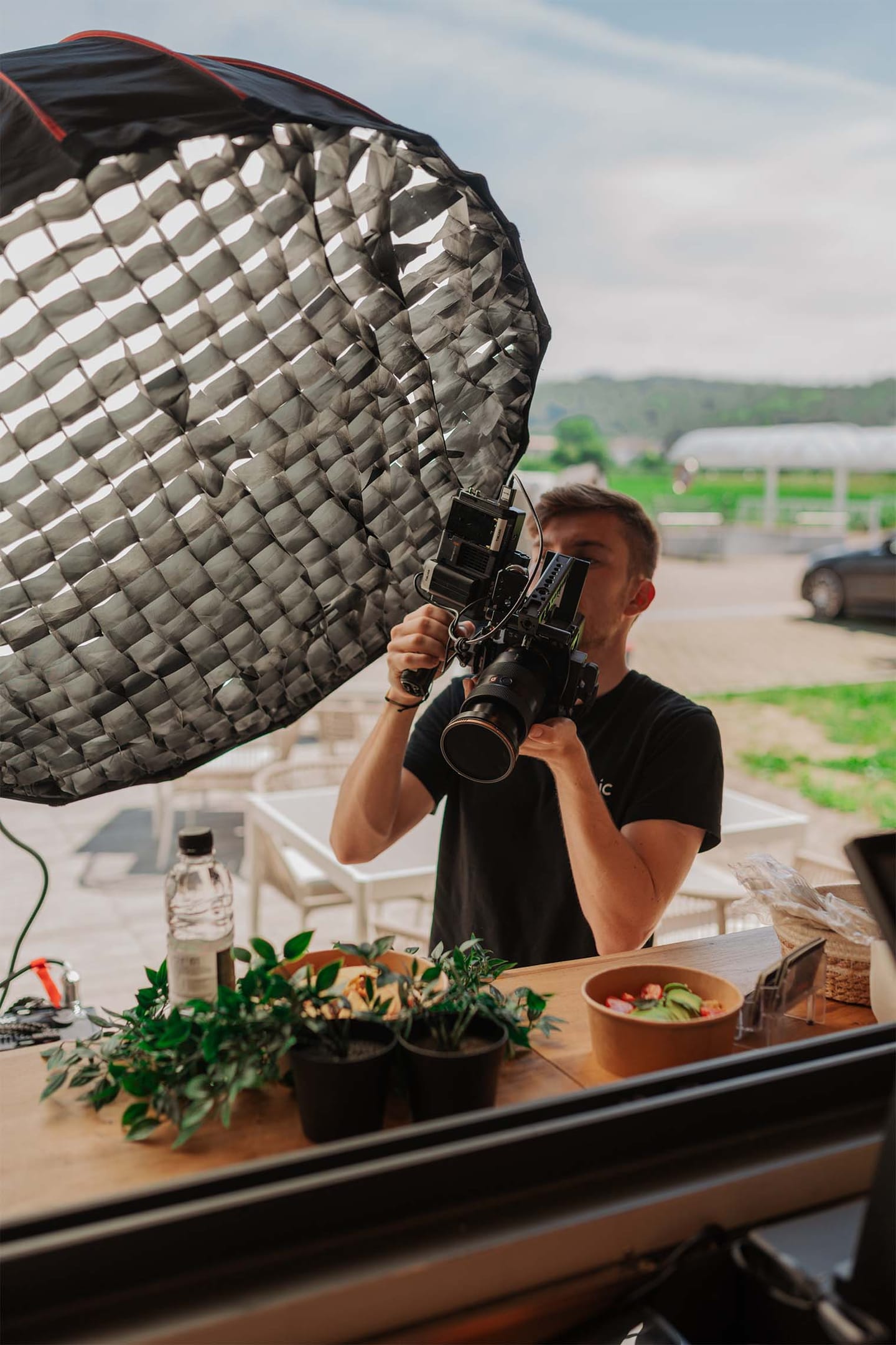 Fotograf s kamero fotografira hrano na mizi ob softboxu.