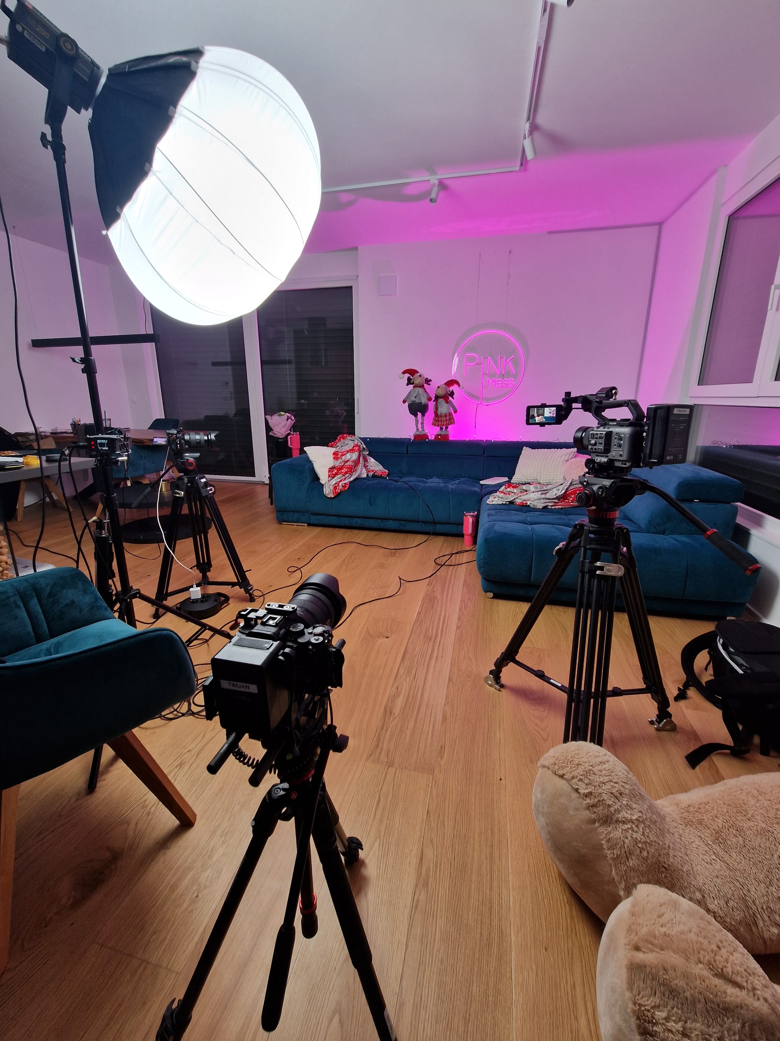 Snemalni studio z lučmi, kamero na stativu in rožnato osvetljenim ozadjem.