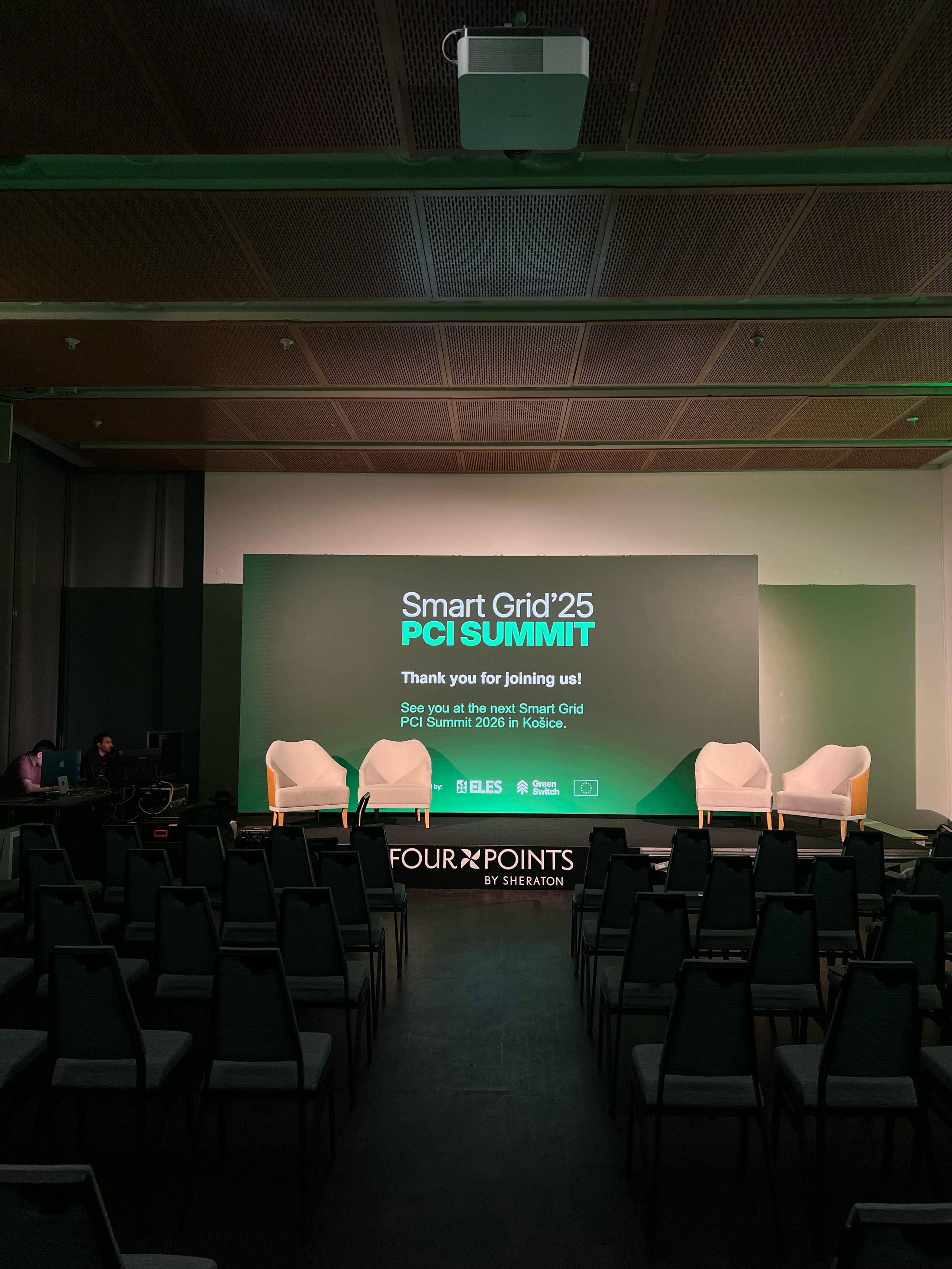 Prazna dvorana z zaslonom Smart Grid Summit in vrstami sedežev.