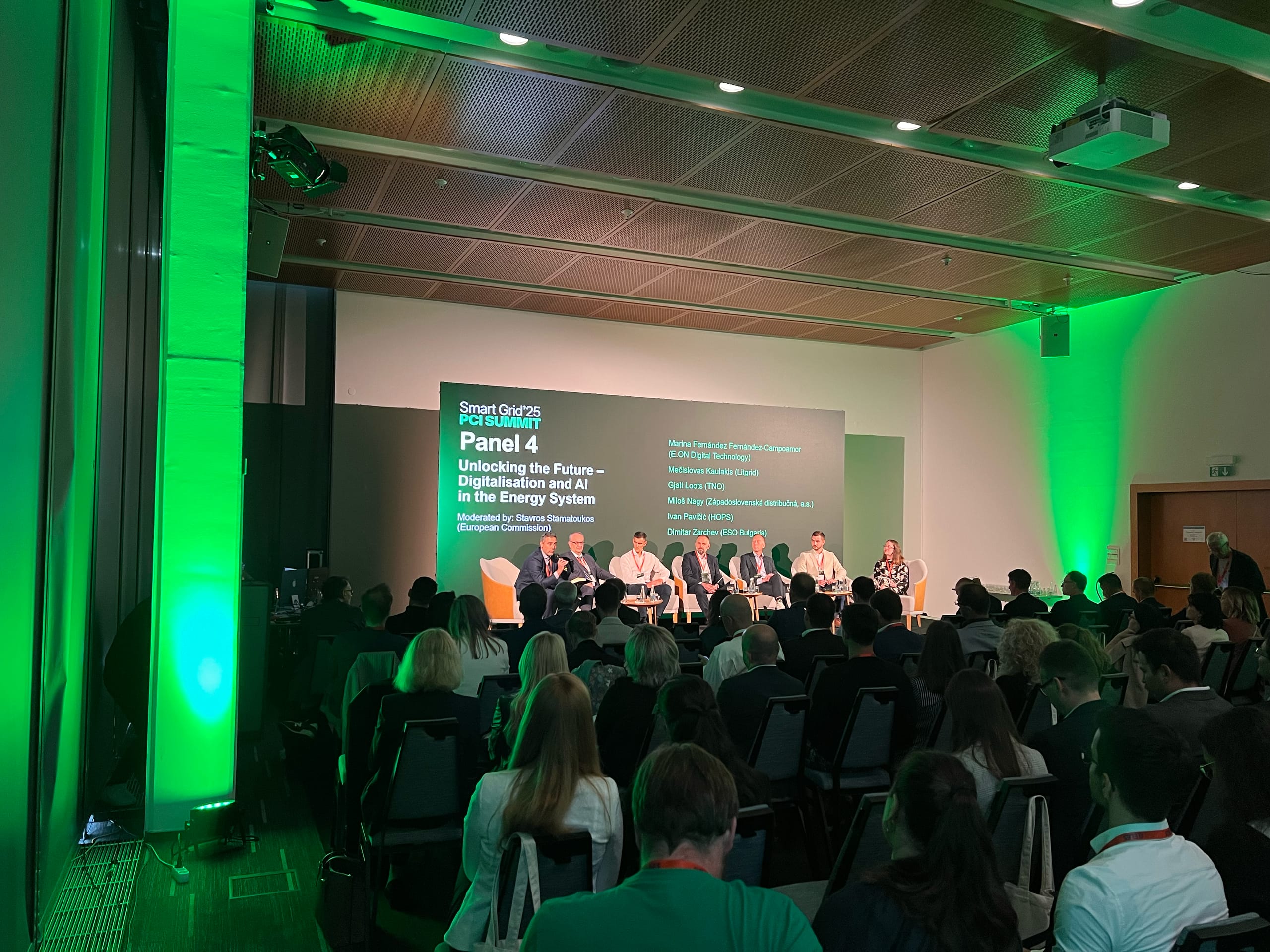 Panelna razprava na konferenci v dvorani z zeleno osvetlitvijo pred občinstvom.