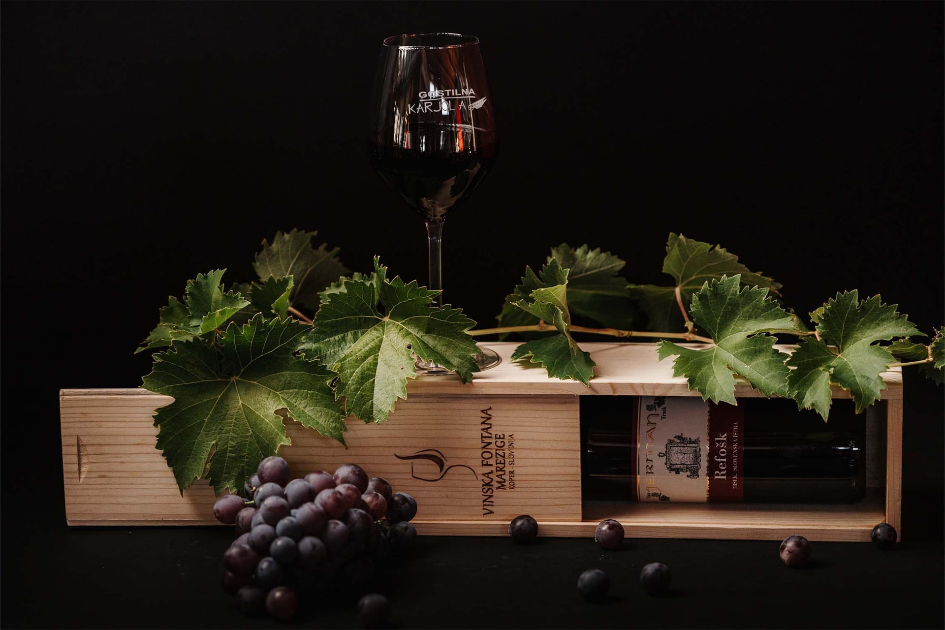 Lesena vinska škatla s kozarcem rdečega vina, grozdjem in vinsko trto.