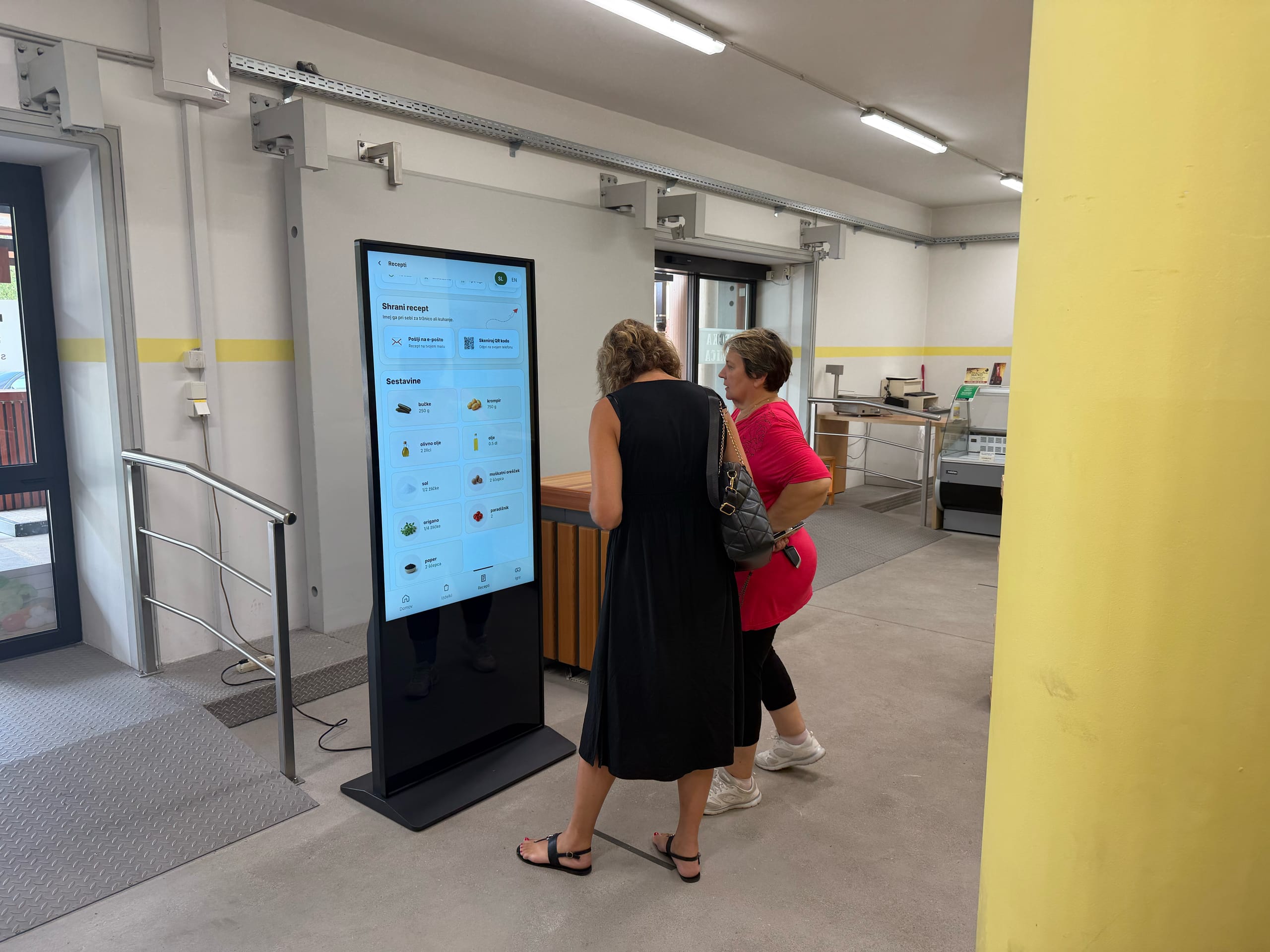 Dve ženski opazujeta digitalni zaslon z informacijami v vhodni avli.