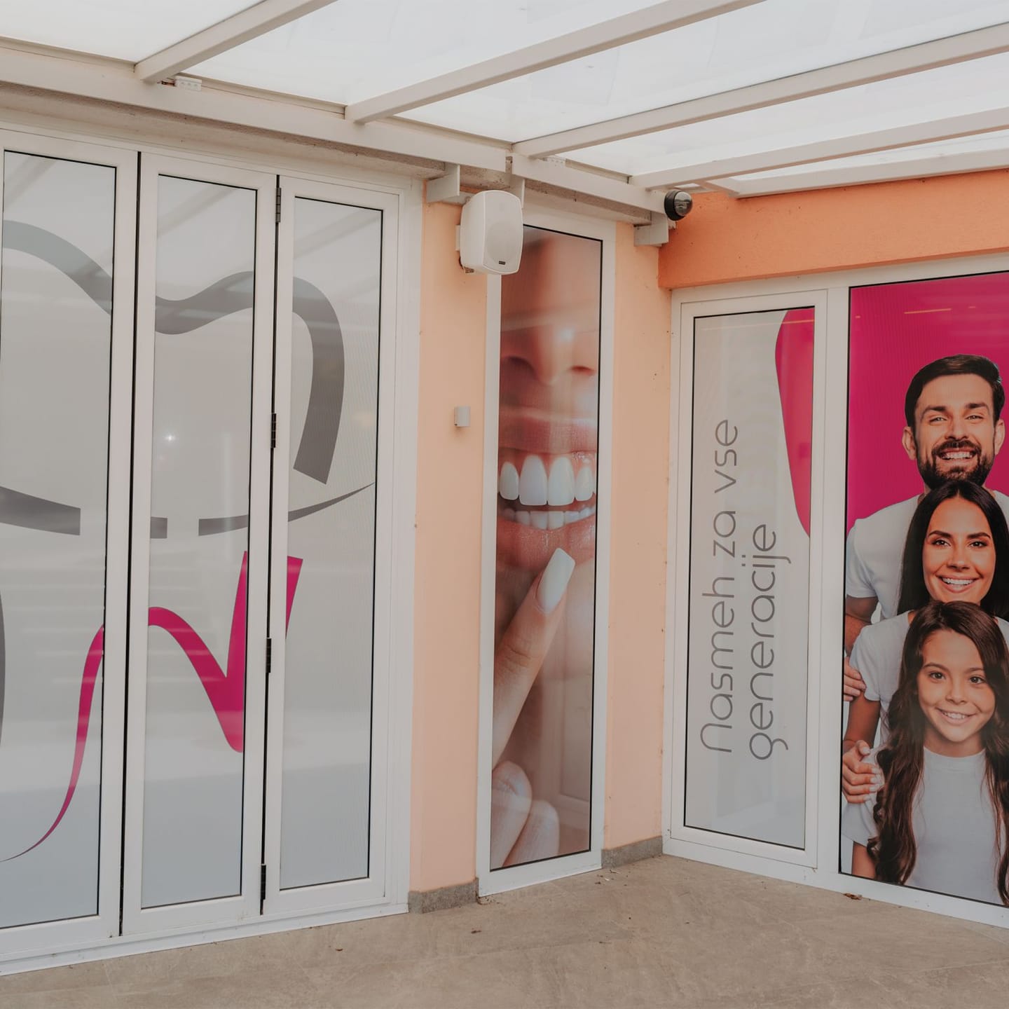 Vhod v zobozdravstveno ordinacijo z reklamnimi nalepkami nasmeha in družine na steklenih vratih.